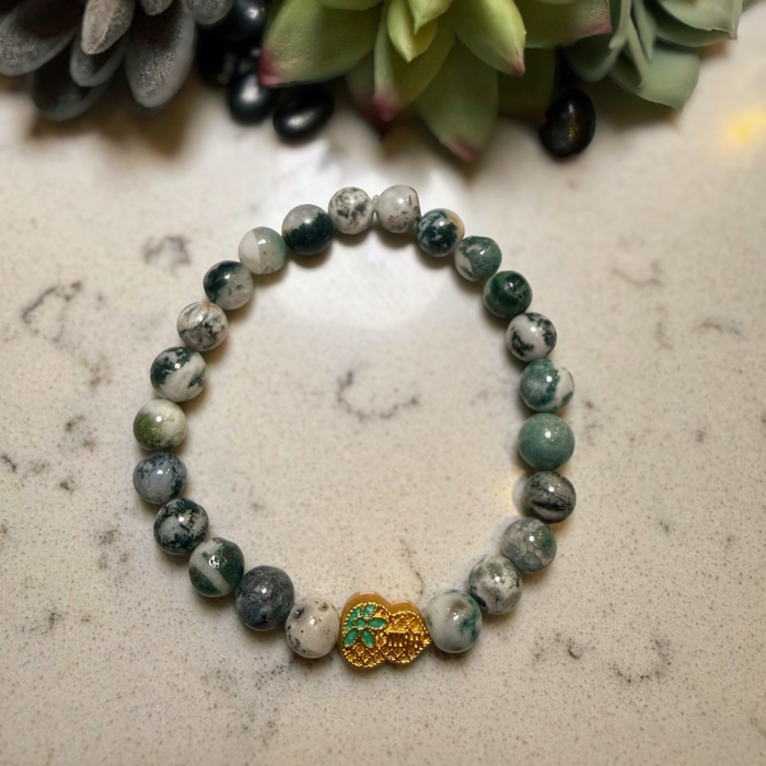 Beaded bracelet with a heart-shaped charm on a marble surface with succulents in the background