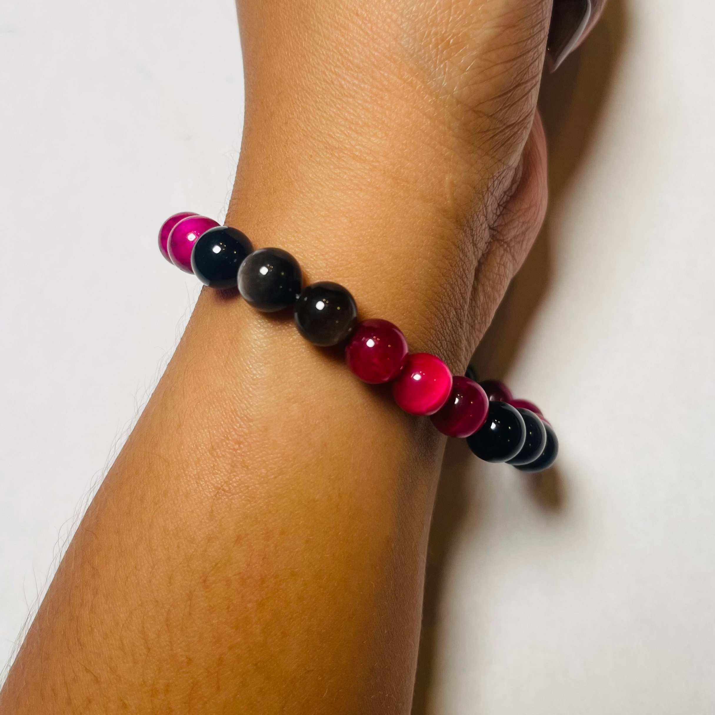 Bracelet with red, black, and pink beads on a wrist against a white background