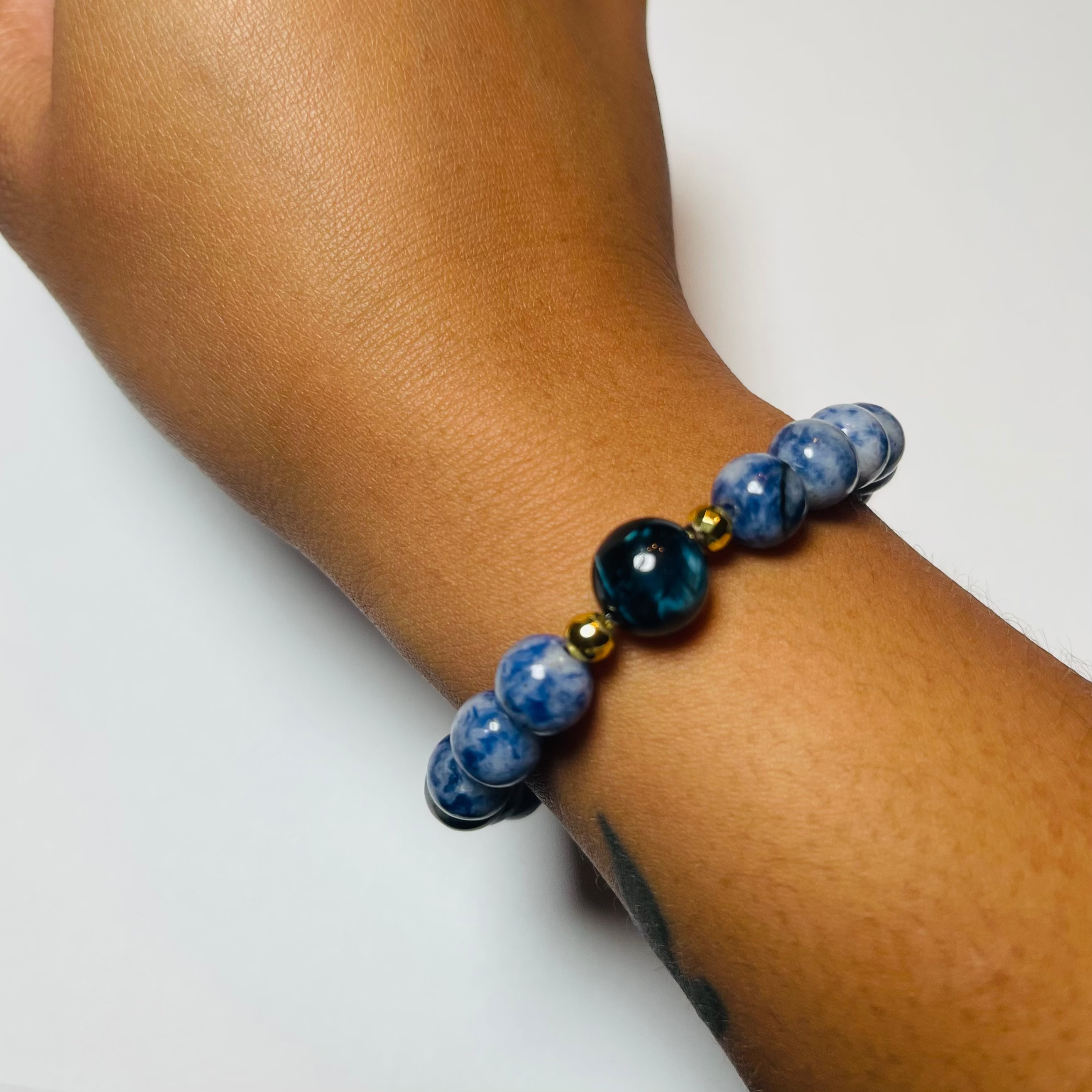 Hand wearing a blue beaded bracelet on a white background