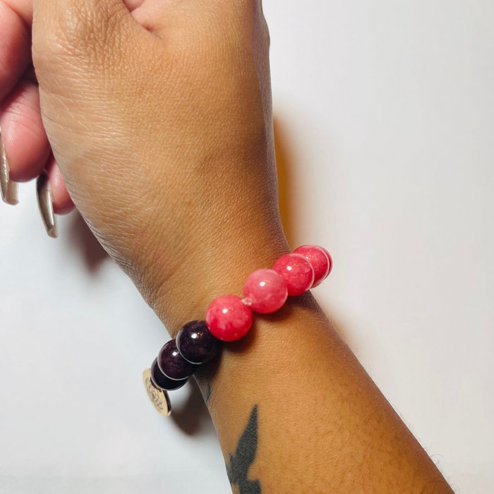 Hand wearing a bracelet with pink and purple beads on a white background