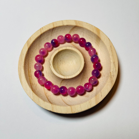 Pink beaded bracelet on a wooden stand against a light gray background