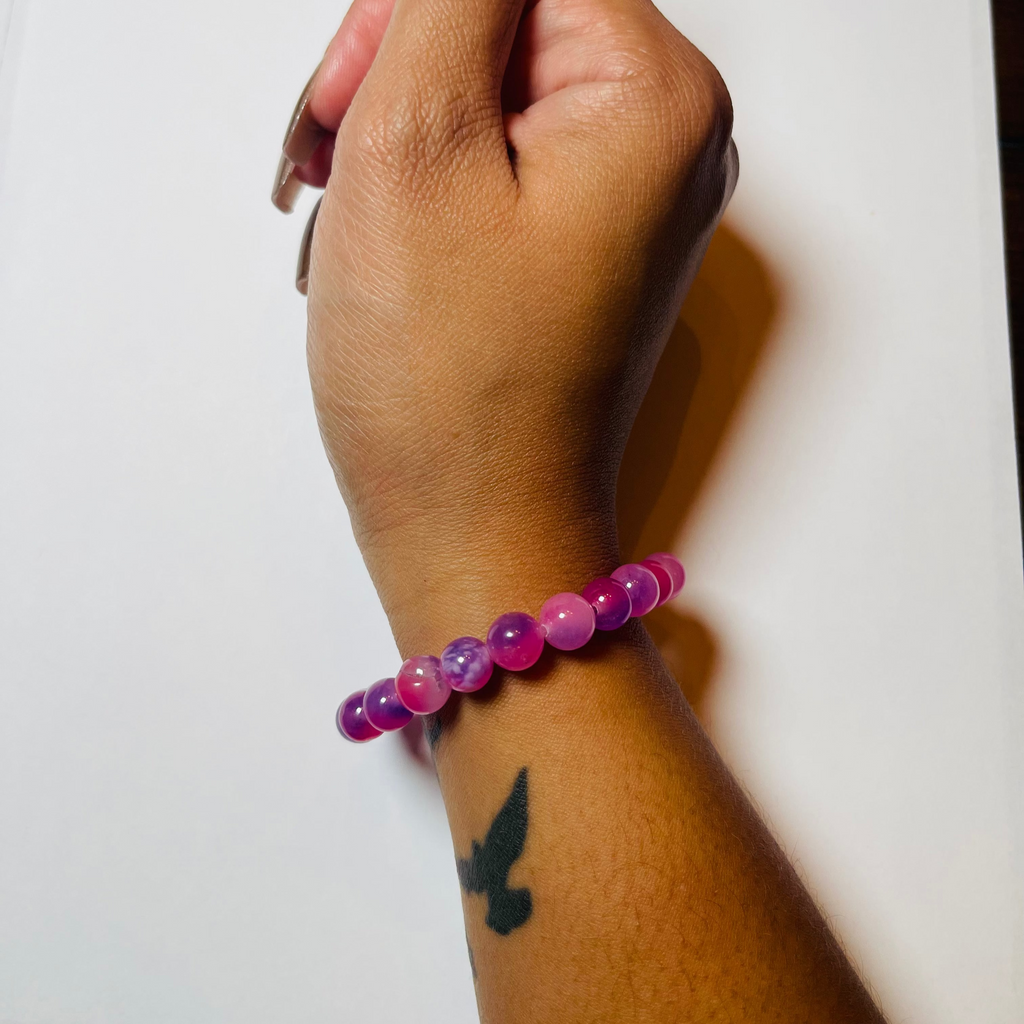 Hand wearing a pink beaded bracelet on a white background
