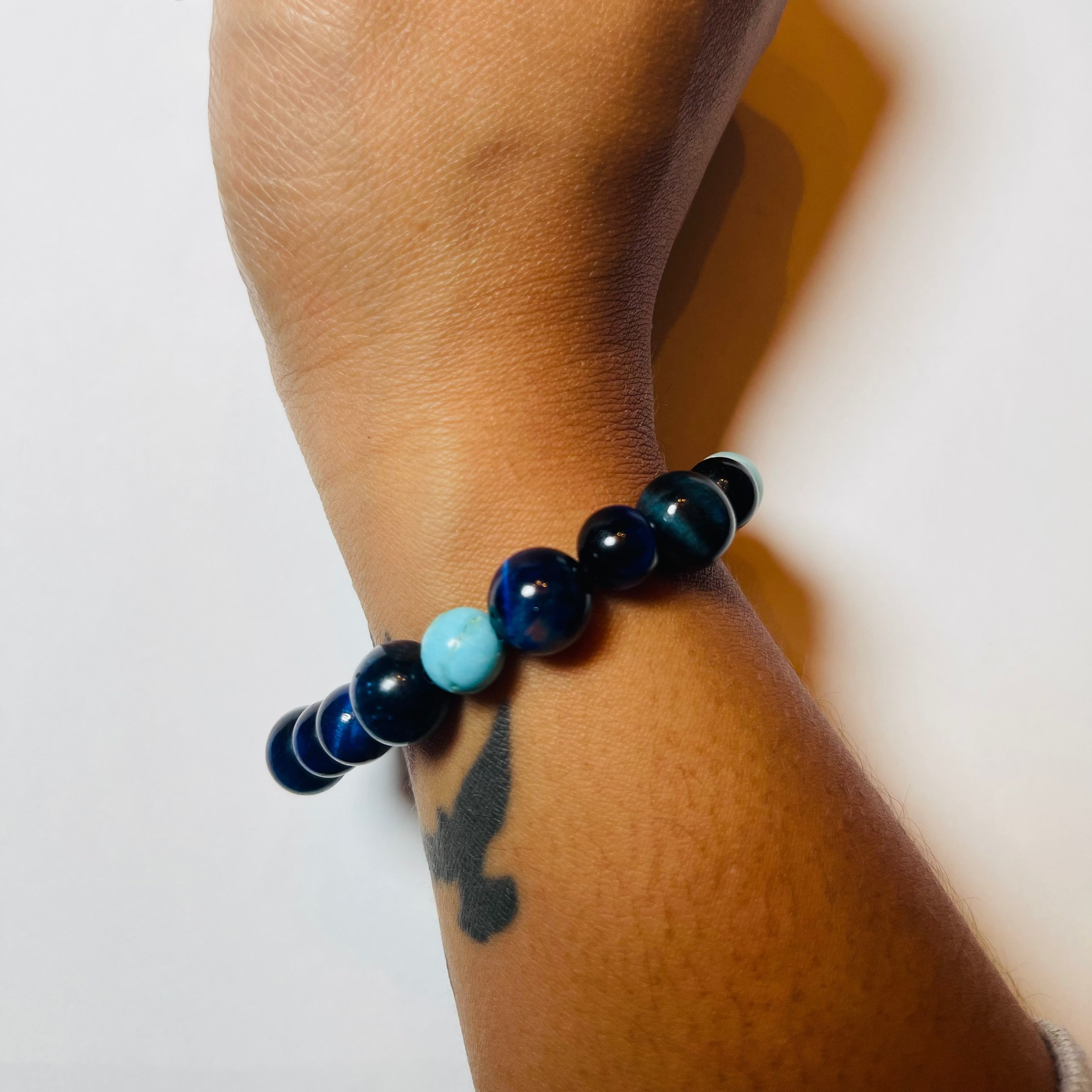 Hand wearing a blue beaded bracelet on a white background