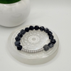 A beaded bracelet with faceted black and white gemstone beads and a silver-toned beaded accent section, displayed on a clear acrylic stand with a white background and a small potted succulent in the upper left.