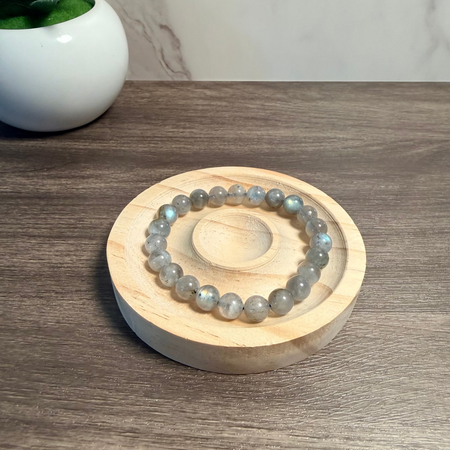 Round wooden coaster with a bracelet on a wooden surface, next to a small potted plant.