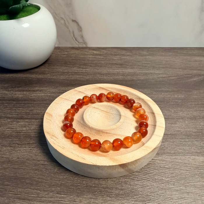 Orange beaded bracelet on a wooden coaster with a white vase in the background