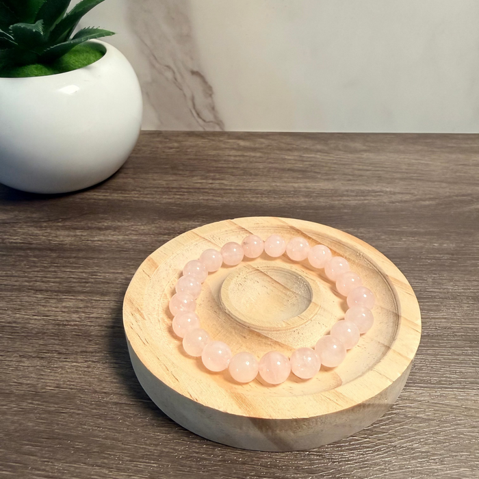 Pnk beaded bracelet on a wooden coaster with a plant in the background