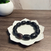Black beaded bracelet on a decorative white dish with a plant in the background