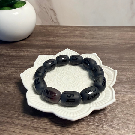 Black beaded bracelet on a decorative white dish with a plant in the background