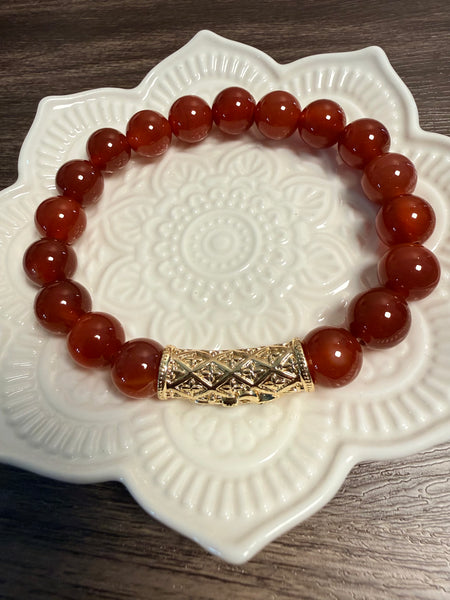 Carnelian beaded bracelet with a gold clasp on a decorative white plate.