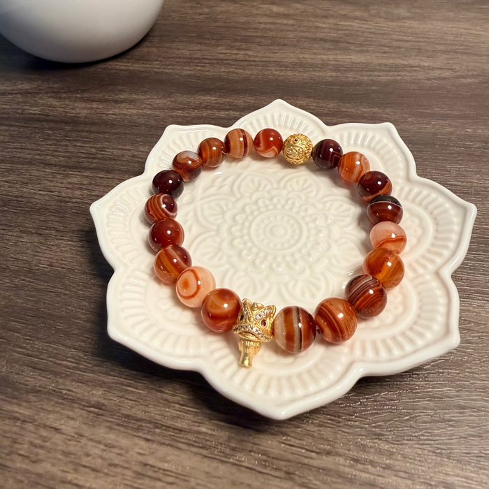 Bracelet with brown and gold beads on a decorative white plate, with a plant in the background.